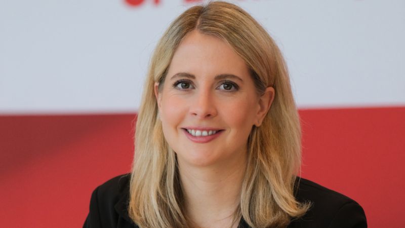 Eine Frau sitzt vor einem SPD-Logo und lächelt in die Kamera.