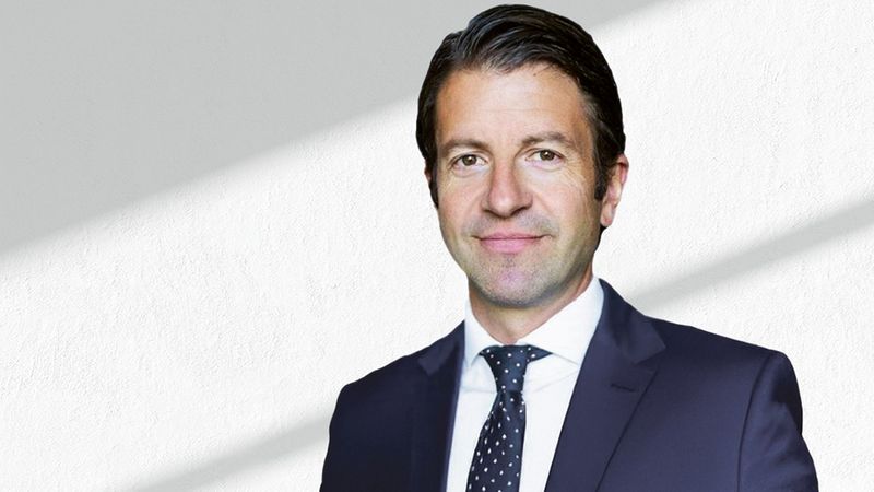 Ein professionelles Portrait eines Geschäftsmannes in einem Anzug vor einem neutralen Hintergrund.