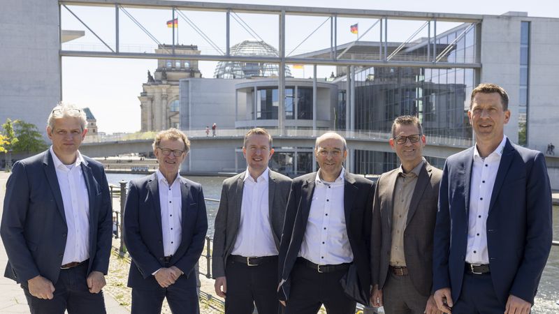 Eine Gruppe von sechs Männern in Anzügen steht vor dem Bundestag in Berlin.