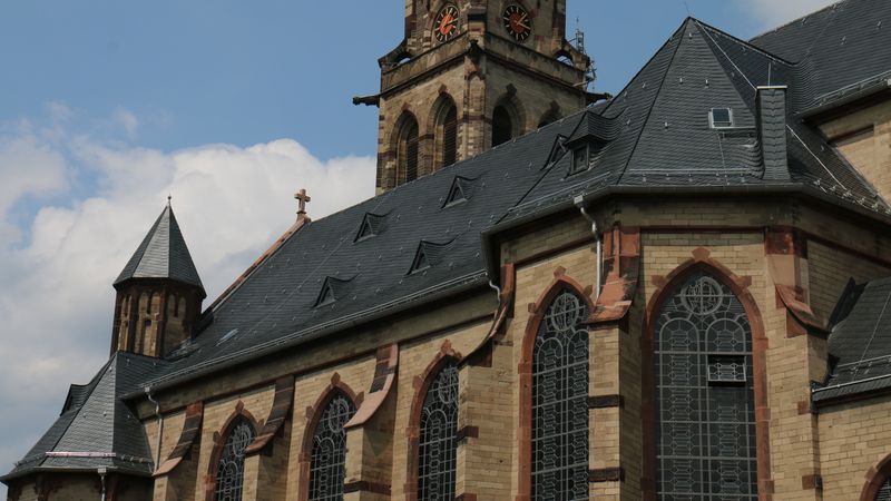 Ein beeindruckendes Beispiel gotischer Architektur mit großen, verzierten Fenstern und einem hohen Turm unter blauem Himmel.