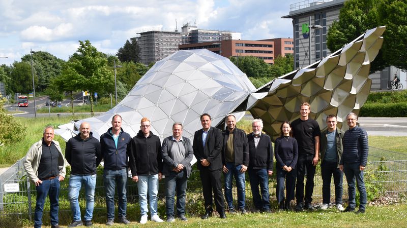 Eine Gruppe von Menschen steht vor einer modernen Skulptur im Freien.