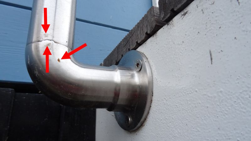 Ein Edelstahlrohr mit einem sichtbaren Riss an einer Ecke, montiert an einer Wand.
