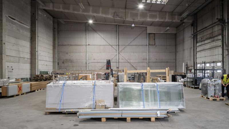 Eine große Lagerhalle mit verpackten Materialien auf Paletten, die in der Mitte des Raumes gestapelt sind.