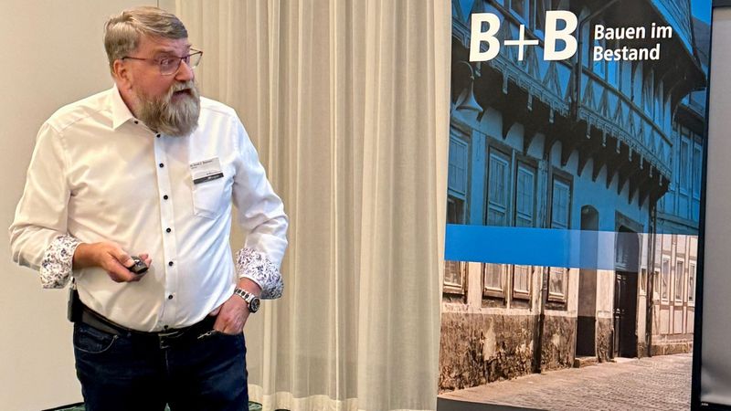 Ein Mann hält eine Präsentation vor einem Roll-Up mit der Aufschrift "Bauen im Bestand".
