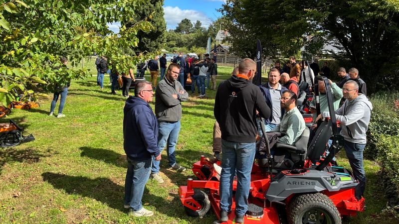 Eine Gruppe von Menschen versammelt sich um einen Aufsitzrasenmäher bei einem Outdoor-Event.