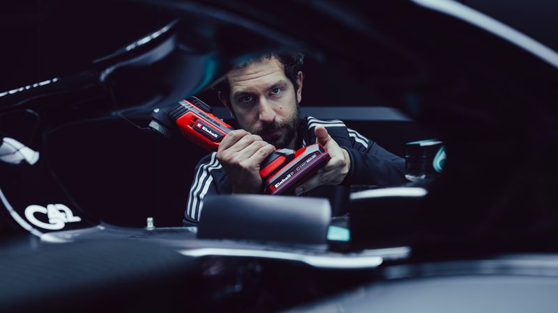 Ein Mechaniker hält ein rotes Elektrowerkzeug in der Hand und arbeitet an einem Fahrzeug.