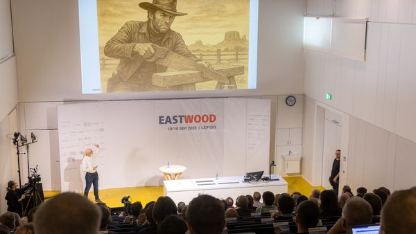 Ein Vortragender präsentiert ein Westernbild in einem Konferenzraum während der EASTWOOD-Veranstaltung in Leipzig.