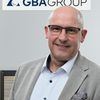 Ein Mann in einem grauen Anzug steht vor einem GBA Group Logo.