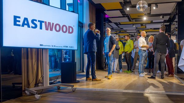 Ein Netzwerktreffen in einem modernen Büro mit mehreren Personen, die sich unterhalten und ein großes Display mit der Aufschrift "EASTWOOD".