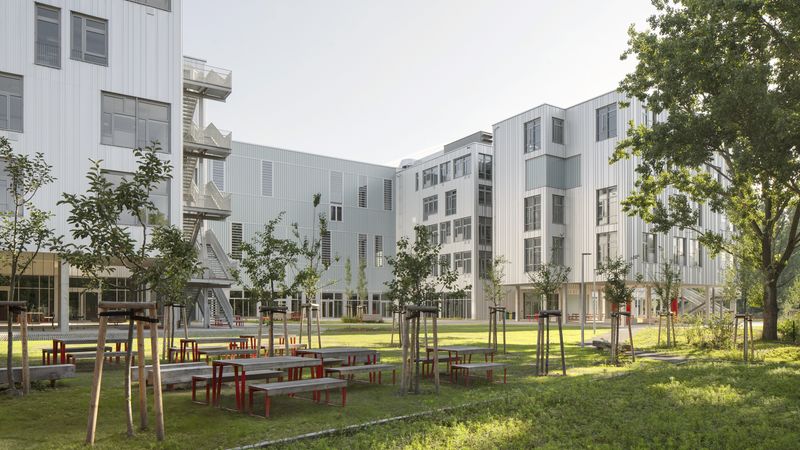 Ein moderner Schulhof mit einer großzügigen Grünanlage und Sitzbänken, umgeben von einem modernen Schulgebäude.