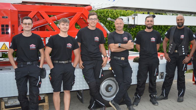 Eine Gruppe von sechs Personen in Arbeitskleidung steht vor einem großen Arbeitsfahrzeug.