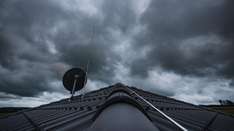 Ein Dach mit einer Satellitenschüssel unter einem dramatischen, bewölkten Himmel.