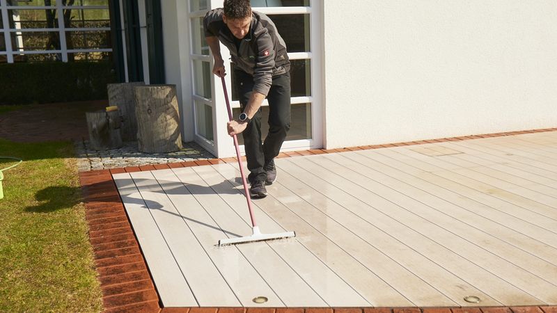 Ein Mann reinigt eine Terrasse mit einem Schrubber an einem sonnigen Tag.