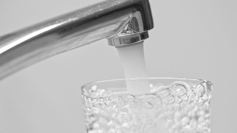 Ein Wasserhahn, der klares Wasser in ein Glas gießt, mit sprudelnden Blasen an der Oberfläche.