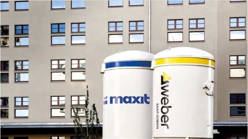 Ein modernes Gebäude mit zwei großen Silos im Vordergrund, die die Logos von Maxit und Weber tragen.