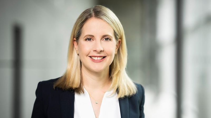 Ein Porträt einer lächelnden Frau in einem professionellen Umfeld.