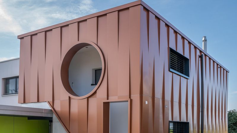 Ein modernes Haus mit einer auffälligen Metallfassade und einem runden Fenster, das sich von der klaren blauen Himmel abhebt.