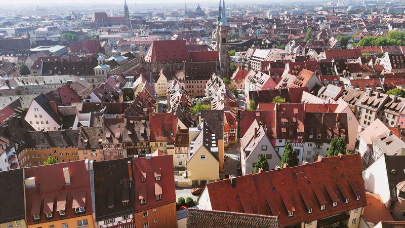 Dieses Bild zeigt einen Panoramablick über die Dächer einer historischen europäischen Altstadt, mit engen Gassen und traditionellen Gebäuden, die sich bis zum Horizont erstrecken.