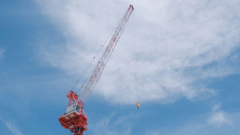 Ein roter Baukran ragt in den blauen Himmel, umgeben von leichten Wolken.