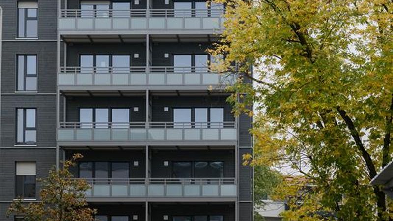 Ein modernes Wohngebäude mit mehreren Balkonen, umgeben von herbstlichen Bäumen und einer Baustelle im Vordergrund.
