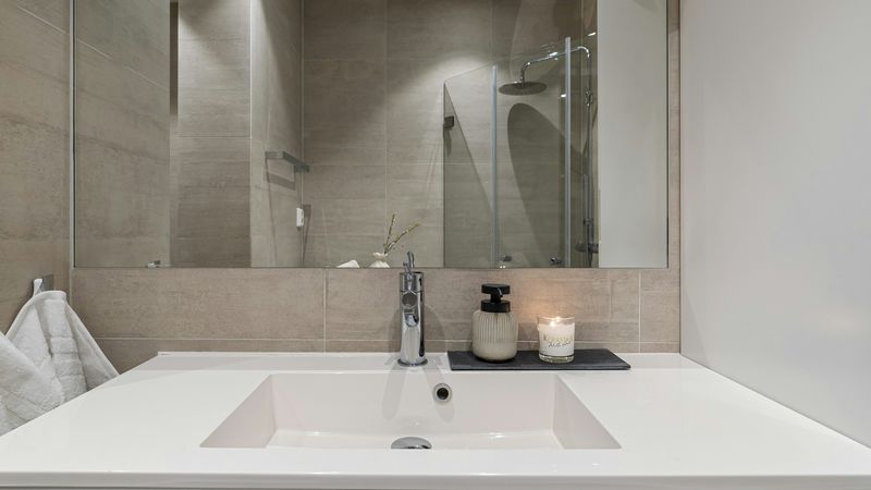 Waschtisch in einem Badezimmer mit beige/grauen Fliesen. Eine Kerze brennt neben dem Seifenspender.