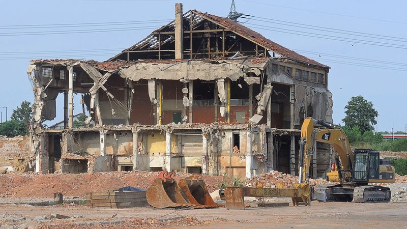Ein teilweise abgerissenes Gebäude auf einer Baustelle mit einem Bagger im Vordergrund.