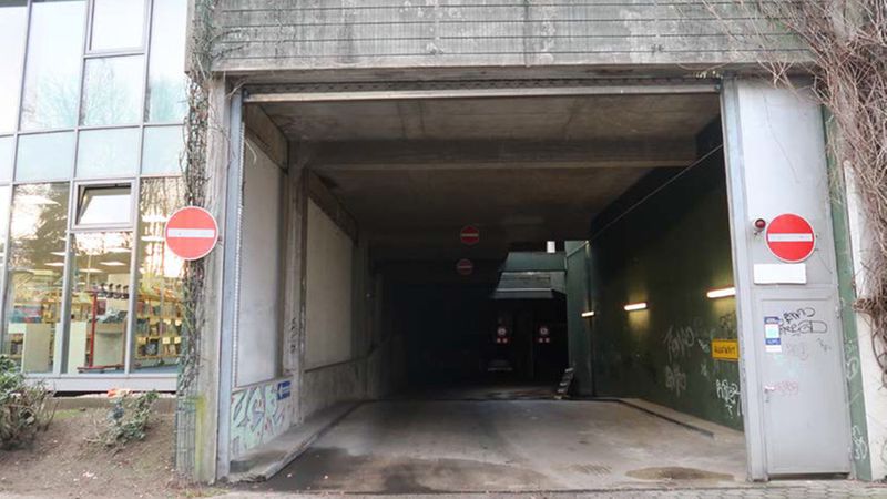 Ein Eingang zu einem Parkhaus mit mehreren Verbotsschildern, die die Einfahrt untersagen. Die Umgebung ist urban mit einem angrenzenden Gebäude.