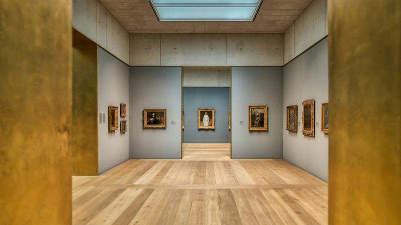 Ein moderner Kunstgalerie-Innenraum mit Holzboden und Gemälden an den Wänden.