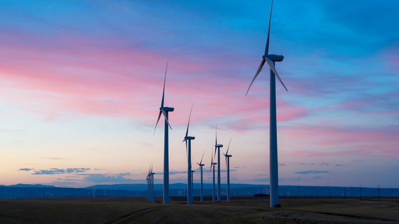 Ein Windpark bei Sonnenuntergang mit mehreren Windkraftanlagen, die sich gegen den farbenfrohen Himmel abheben.