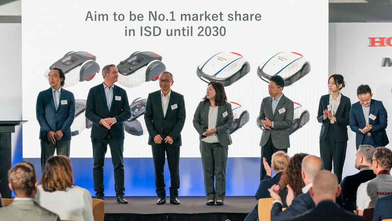 Eine Gruppe von Personen steht auf einer Bühne vor einem Bildschirm, der eine Präsentation von Robotern zeigt.