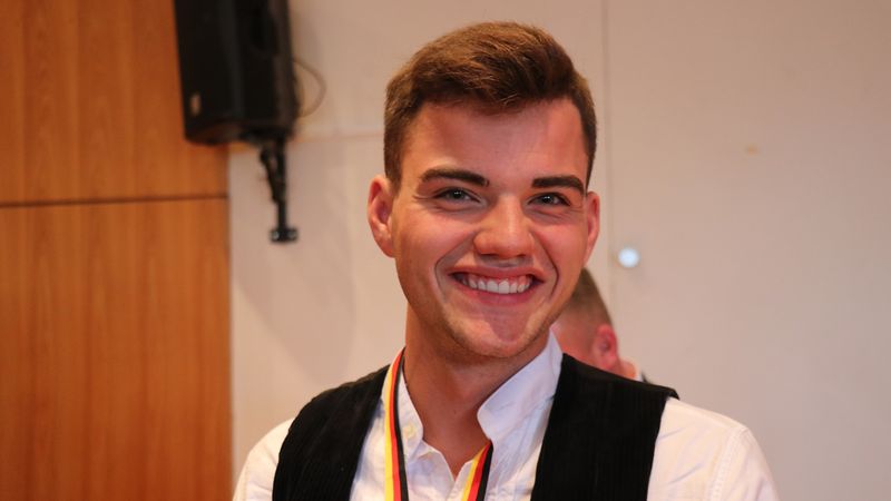 Ein junger Mann lächelt in die Kamera und trägt eine Medaille um den Hals.