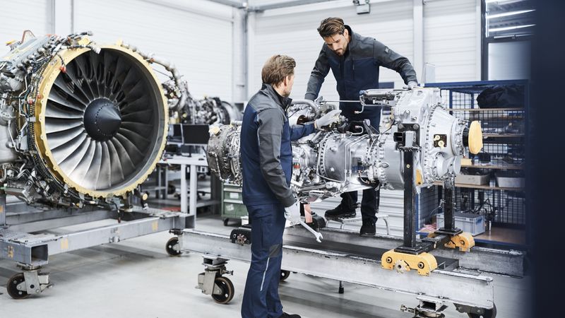 Zwei Männer in Arbeitskleidung arbeiten an einer Turbine in einer Halle.