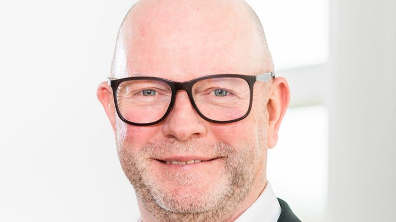 Ein Porträt eines lächelnden Mannes mit Brille in einem Anzug.