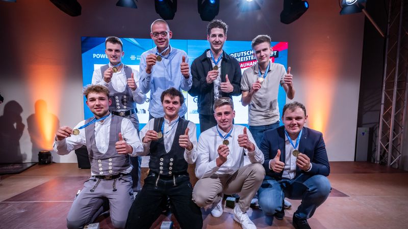 Eine Gruppe von Handwerkern posiert stolz mit Medaillen auf einer Bühne.