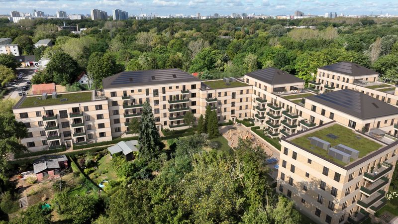 Eine moderne Wohnanlage mit Dachbegrünung, umgeben von üppiger Vegetation und städtischer Landschaft im Hintergrund.