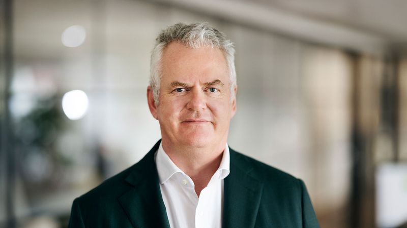 Ein Mann mittleren Alters in einem dunklen Anzug steht in einem modernen Büro.