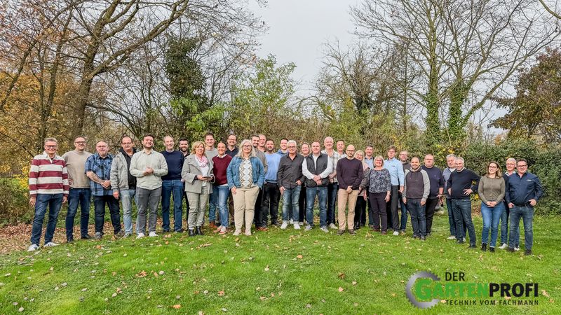 Eine Gruppe von Menschen steht auf einer Wiese in einem herbstlichen Garten.