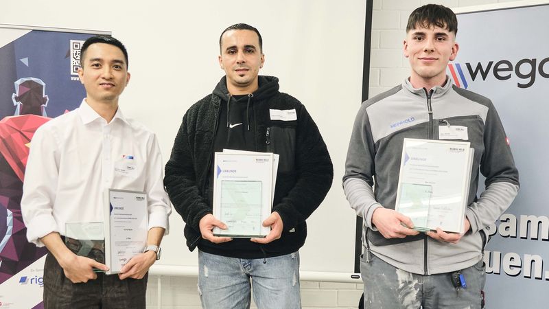 Drei Männer stehen auf einem Siegerpodest und halten Zertifikate in den Händen.