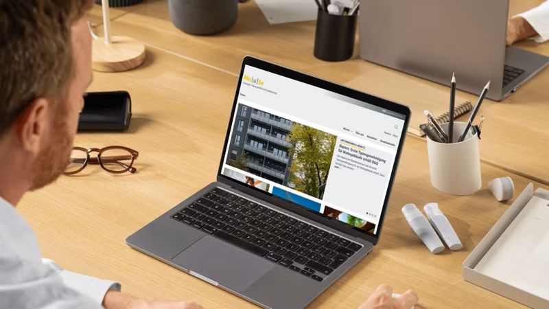 Ein Mann sitzt an einem Schreibtisch und betrachtet einen Laptop im Büro.