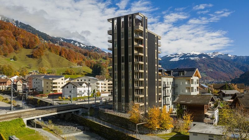 Ein modernes Hochhaus in einer malerischen Berglandschaft mit herbstlichen Farben.