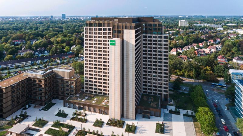 Ein modernes Hochhaus im Stadtzentrum, umgeben von Grünflächen und weiteren Gebäuden.