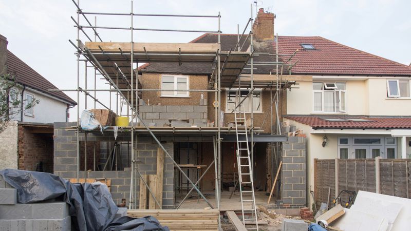 Ein Haus im Renovierungsprozess mit einem Gerüst an der Fassade und Baumaterialien im Vordergrund.