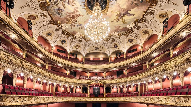 Ein prächtiges Theaterinterieur mit einem kunstvoll verzierten Deckengemälde und einem großen Kronleuchter.