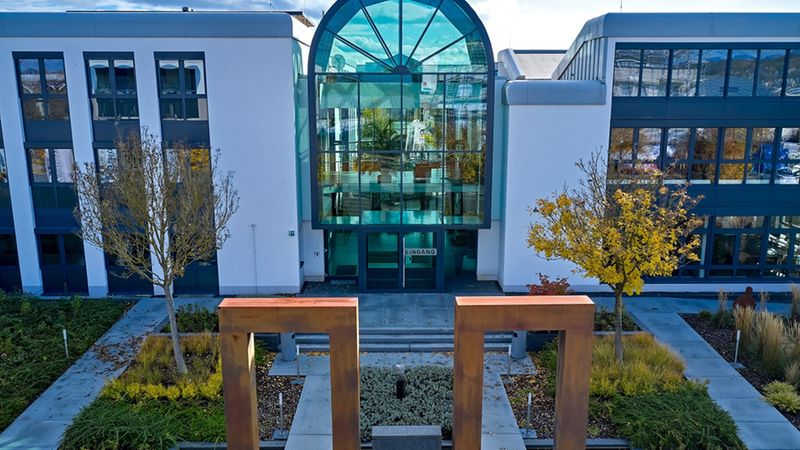 Ein modernes Bürogebäude mit Glasfassade und geometrischen Skulpturen im Vordergrund.