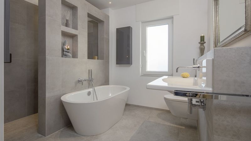 Ein modernes Badezimmer mit einer freistehenden Badewanne, grauen Fliesen und stilvoller Dekoration.