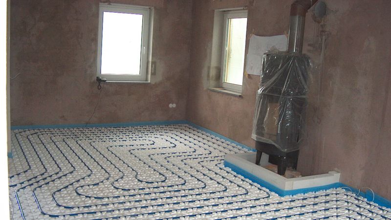 Installation einer Fußbodenheizung in einem leeren Raum mit unverputzten Wänden.