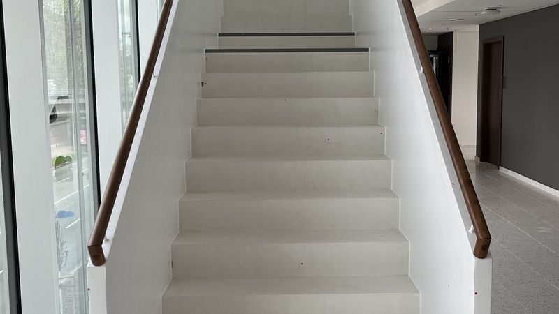 Eine moderne, weiße Treppe in einem Bürogebäude mit einem Aktenordner auf der untersten Stufe.