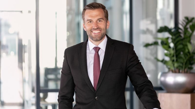 Ein lächelnder Geschäftsmann im Anzug steht in einem modernen Büro.