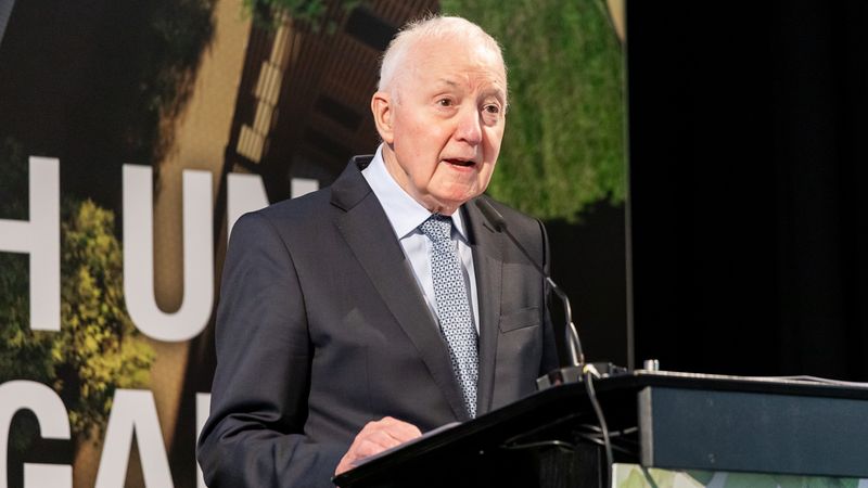 Ein älterer Mann in einem Anzug hält eine Rede an einem Podium.