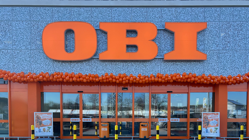 Eingang eines Baumarkts mit großen orangefarbenen Buchstaben und Luftballons.